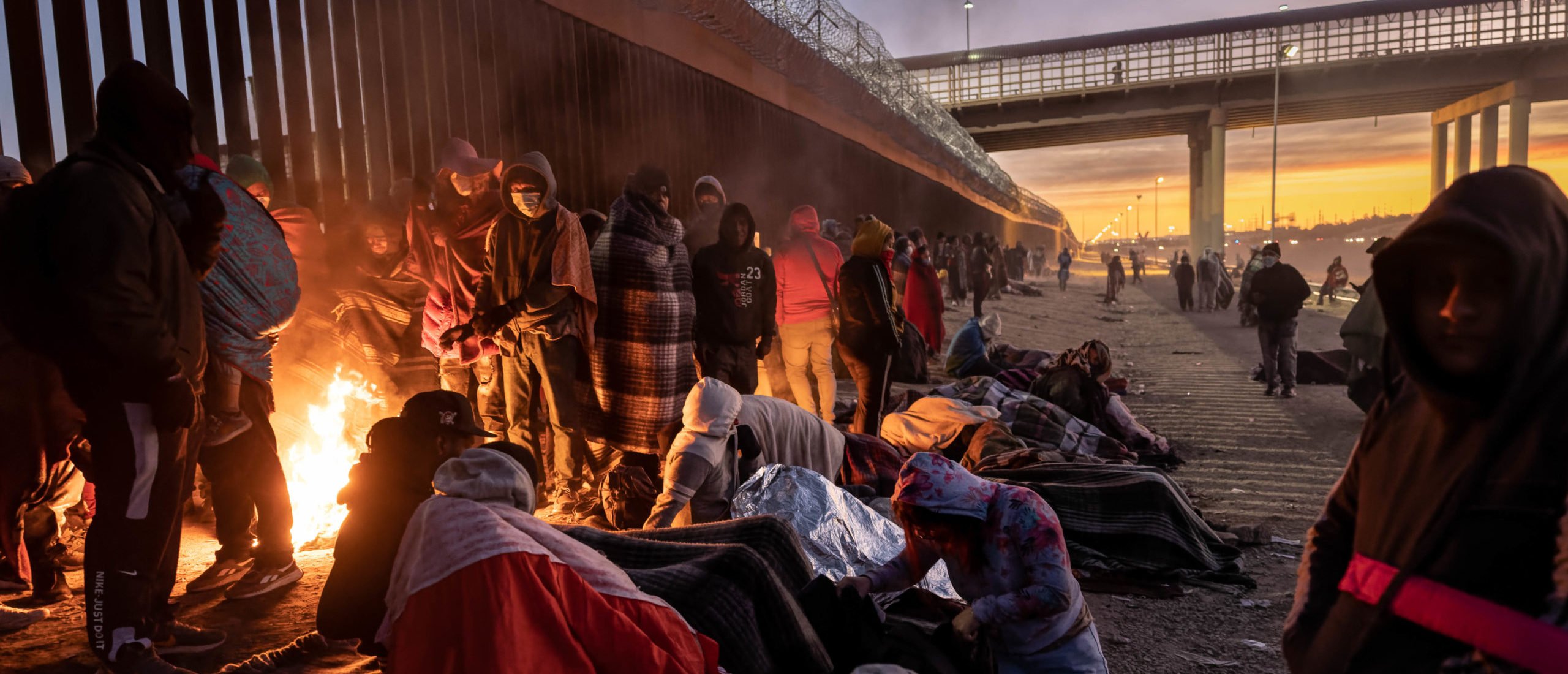EL PASO, TEXAS - DECEMBER 22: Immigrants warm to a fire at dawn after spending the night outside next to the U.S.-Mexico border fence on December 22, 2022 in El Paso, Texas. A spike in the number of migrants seeking asylum in the United States has challenged local, state and federal authorities. The numbers are expected to increase as the fate of the Title 42 authority to expel migrants remains in limbo pending a Supreme Court decision expected after Christmas. (Photo by John Moore/Getty Images)