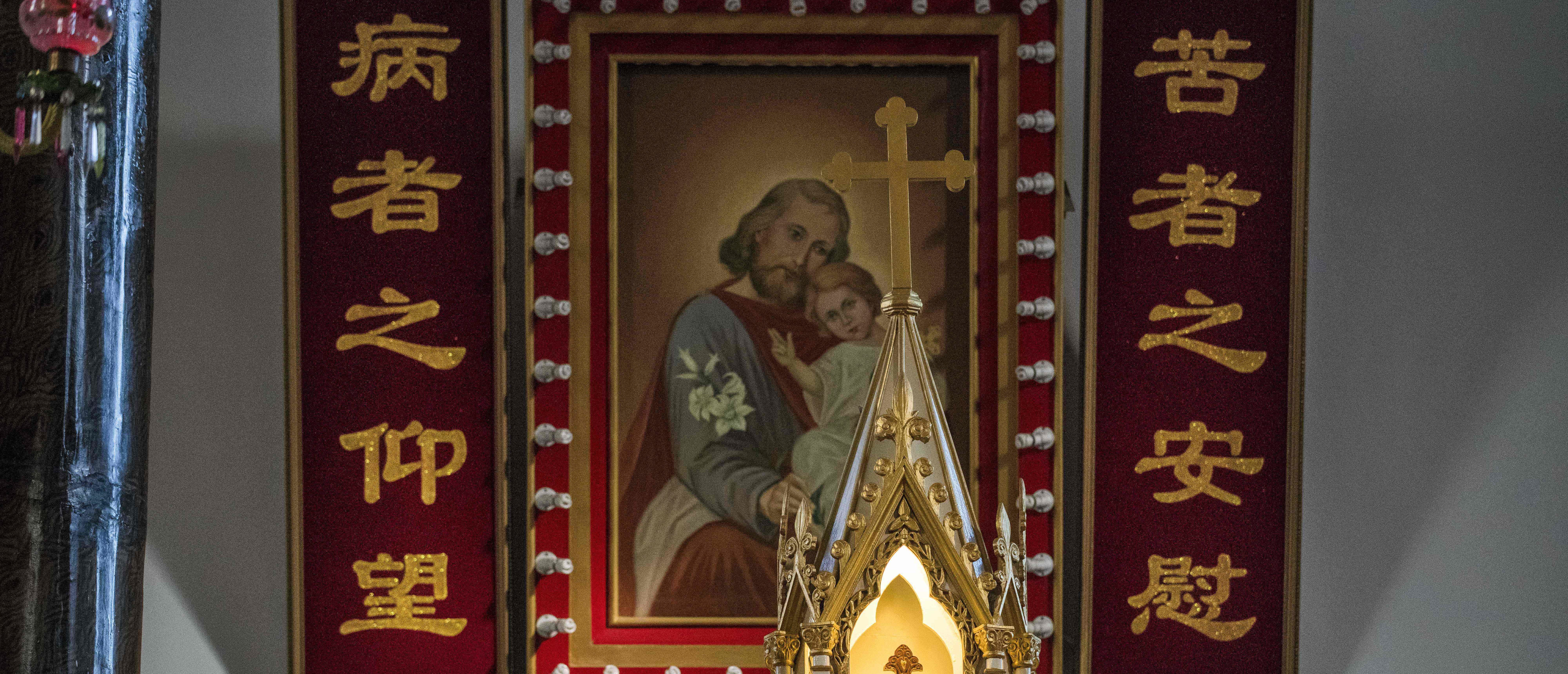 A cross with Jesus (front) and a painting with Joseph and Jesus (back) are seen inside St. Joseph's church, also known as Wangfujing church, in Beijing on January 25, 2018. [NICOLAS ASFOURI/AFP via Getty Images]