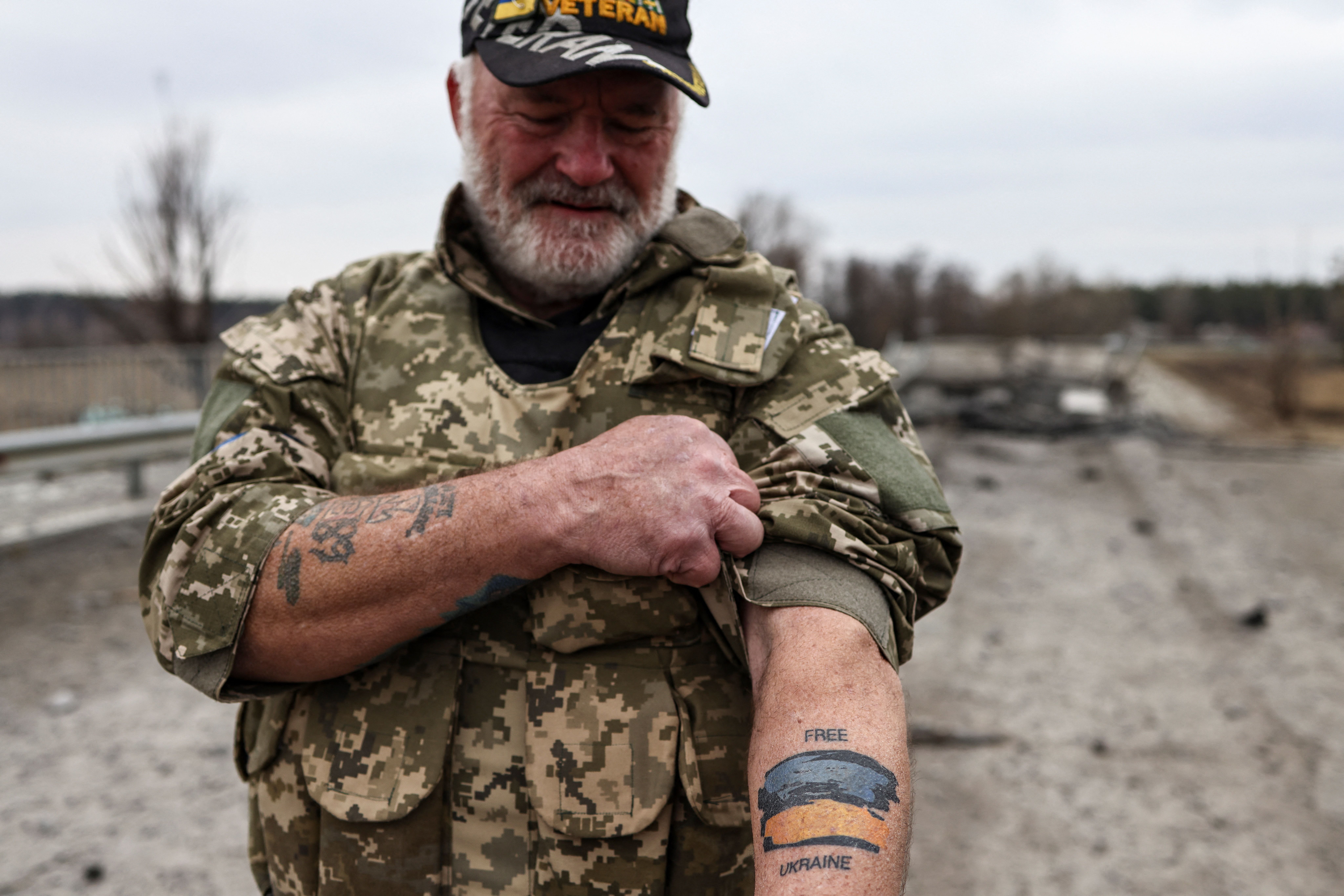 TOPSHOT - US war veteran Steven Straub shows his tattoo with the Ukranian flag as they patrol on a road near Buda-Babynetska, north of Kyiv, on April 5, 2022, days after Russian forces retreated from the area