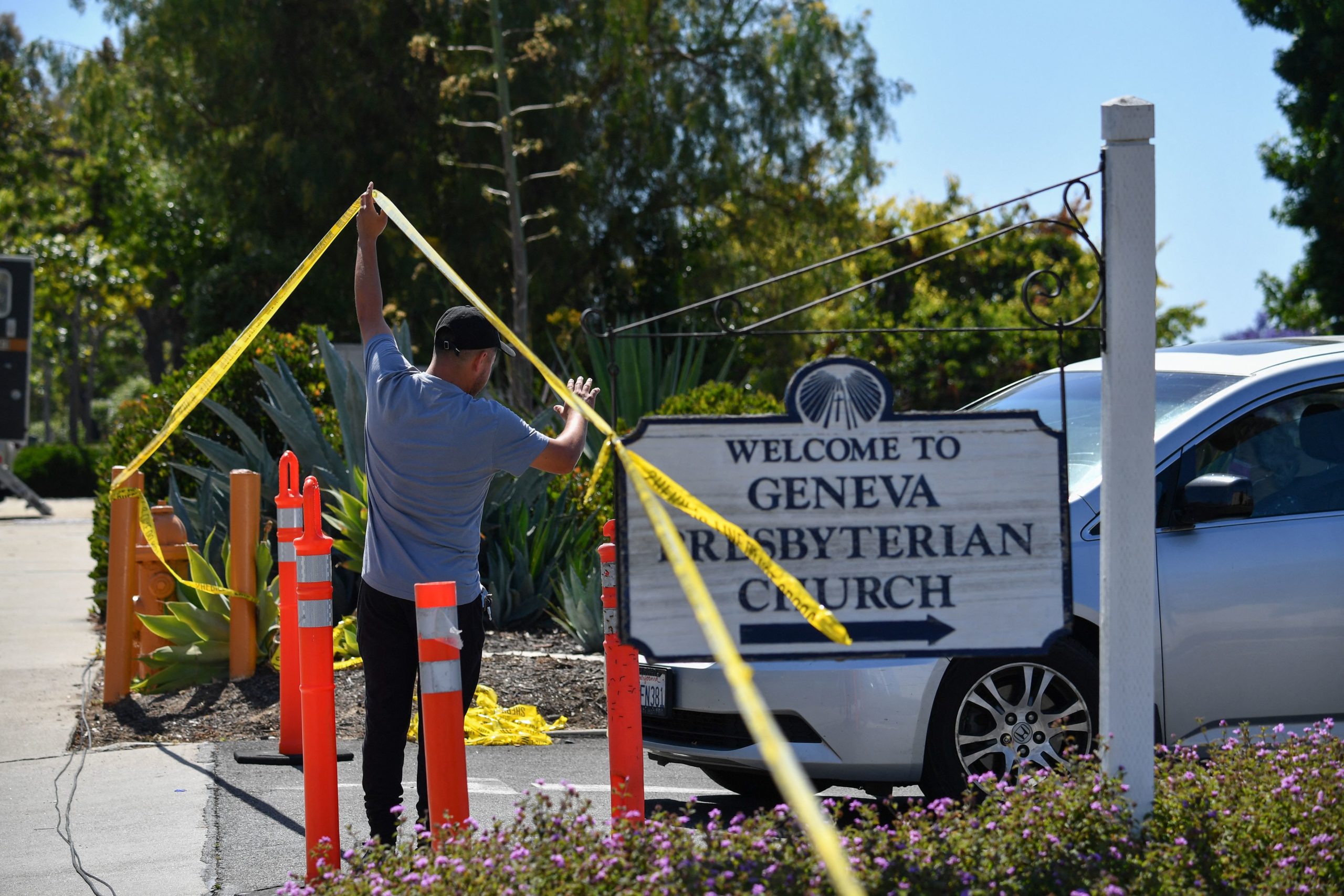 A church staff member raises police tape for a car to exit at the Geneva Presbyterian Church May 16, 2022 after one person was killed and five injured during a shooting May 15, 2022 at the church in Laguna Woods, California. - A Chinese immigrant who padlocked a church and opened fire on its Taiwanese-American congregation, killing one person and injuring five others, was motivated by hatred of the island and its people, US investigators said May 16. (Photo by Robyn Beck / AFP) (Photo by ROBYN BECK/AFP via Getty Images)