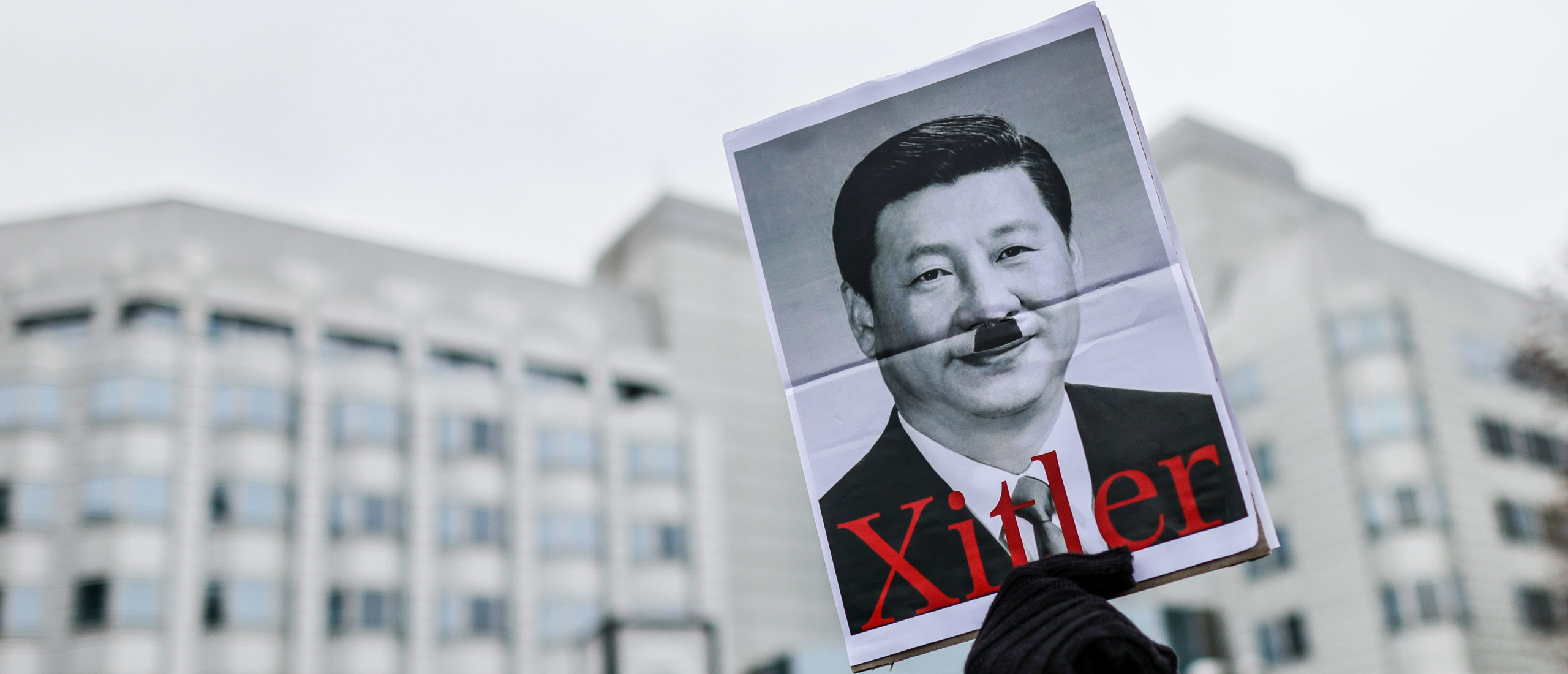 A protester holds a picture of Xi Jinping with a "Hitler moustache" in Germany in 2022. (Photo by Omer Messinger/Getty Images)