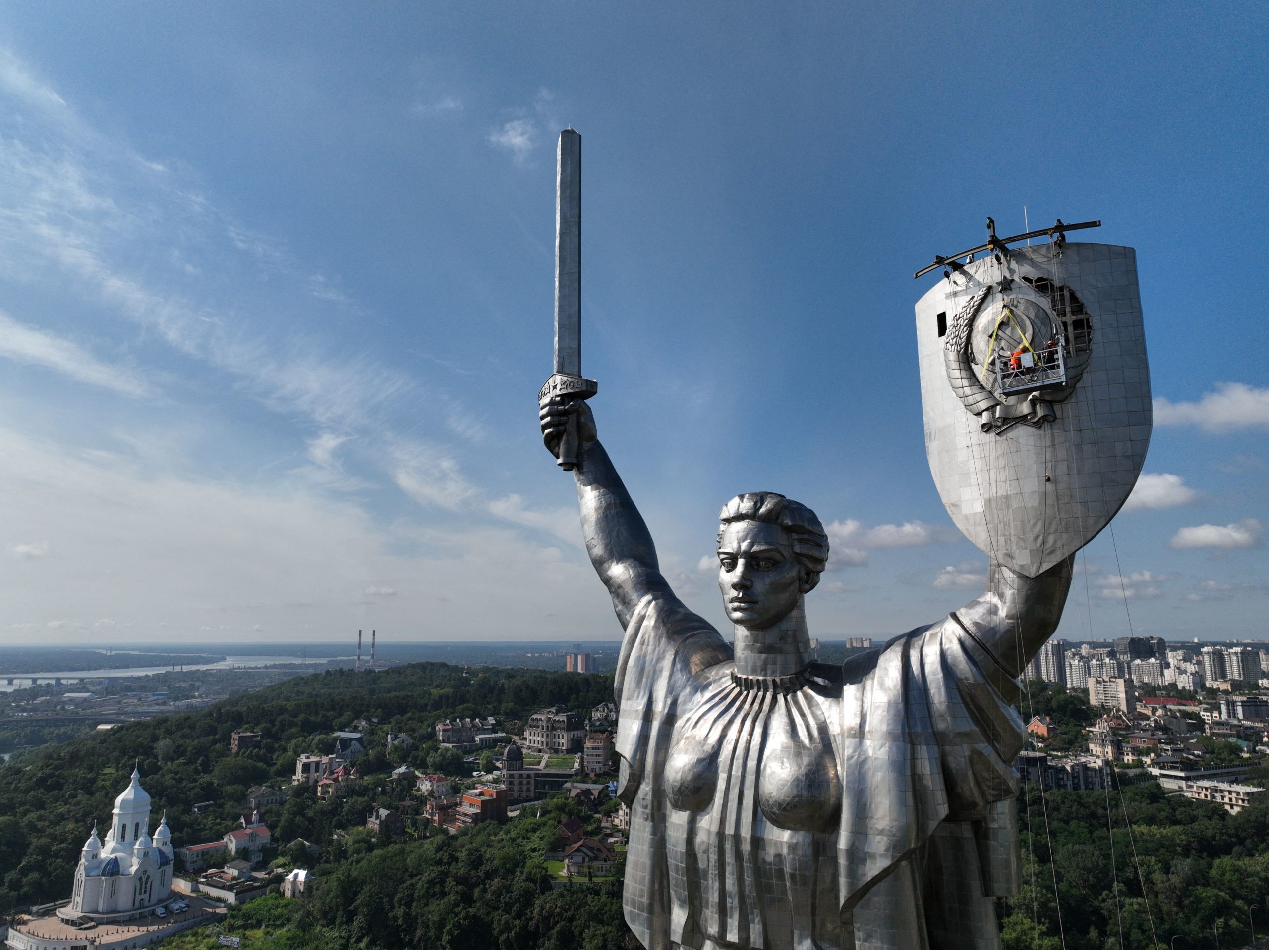 This aerial view taken on August 1, 2023, shows the Motherland Monument as steeplejacks dismantle the coat of arms of the former Soviet Union from the shield of a 62-meter (102 meters with pedestal) Motherland Monument in Kyiv, amid the Russian invasion of Ukraine. Workers in a cradle suspended from a rail on top of the shield have been gradually cutting off grain and ribbon elements of the Soviet emblem and lowering them on ropes for a month now. Finally, the whole shield will be replaced with a new one bearing the trident. (Photo by Sergii VOLSKYI / AFP) (Photo by SERGII VOLSKYI/AFP via Getty Images)