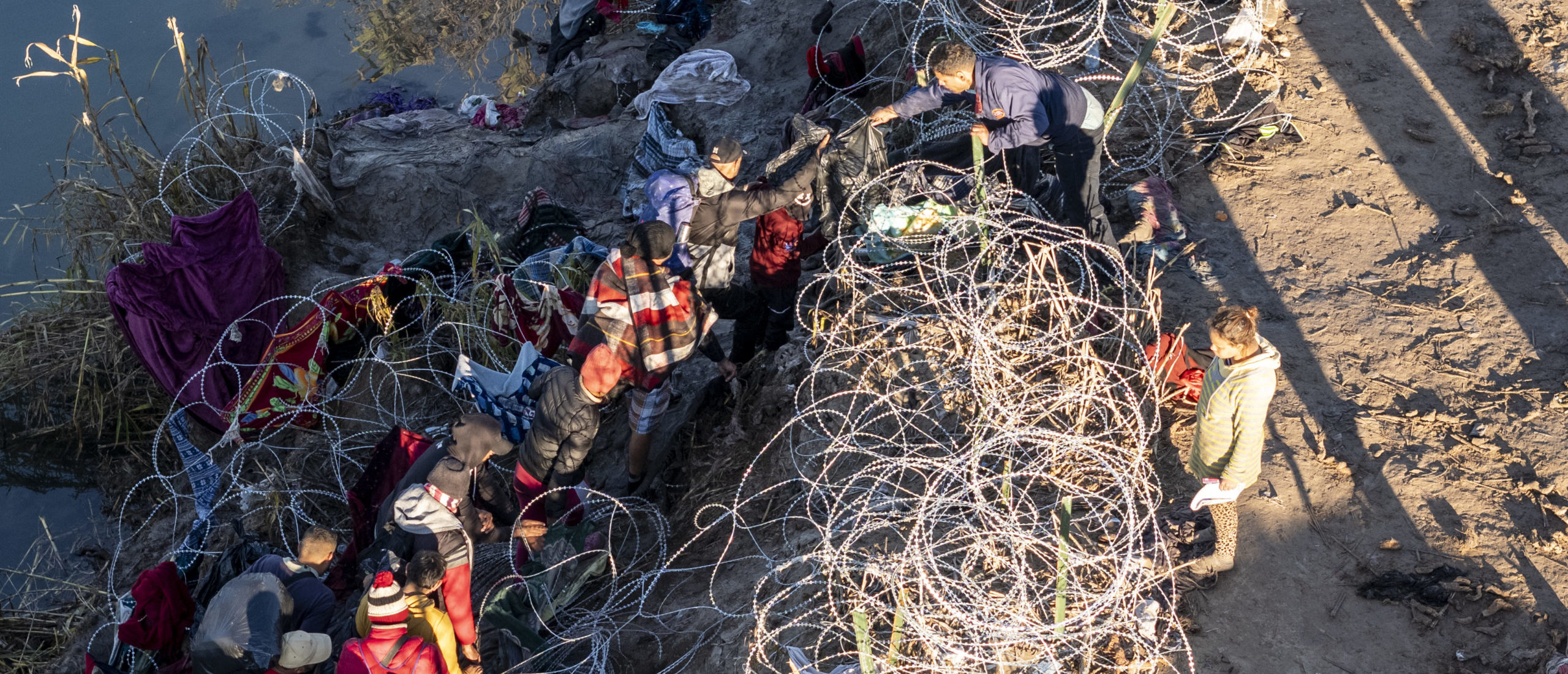 EAGLE PASS, TEXAS - DECEMBER 18: As seen from an aerial view immigrants climb through razor wire after crossing the Rio Grande from Mexico on December 18, 2023 in Eagle Pass, Texas. A surge as many as 12,000 immigrants per day crossing the U.S. southern border has overwhelmed U.S. immigration authorities in recent weeks. (Photo by John Moore/Getty Images)