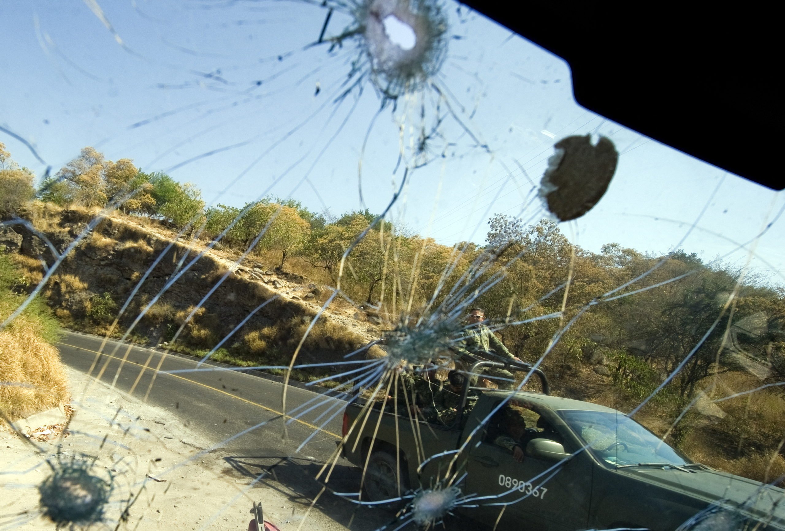Mexican Army soldiers passing by are seen through the bullet-riddled windshield of a truck in Apatzingan, Michoacan State, Mexico, on December 12, 2010. (Photo by ALFREDO ESTRELLA/AFP via Getty Images)