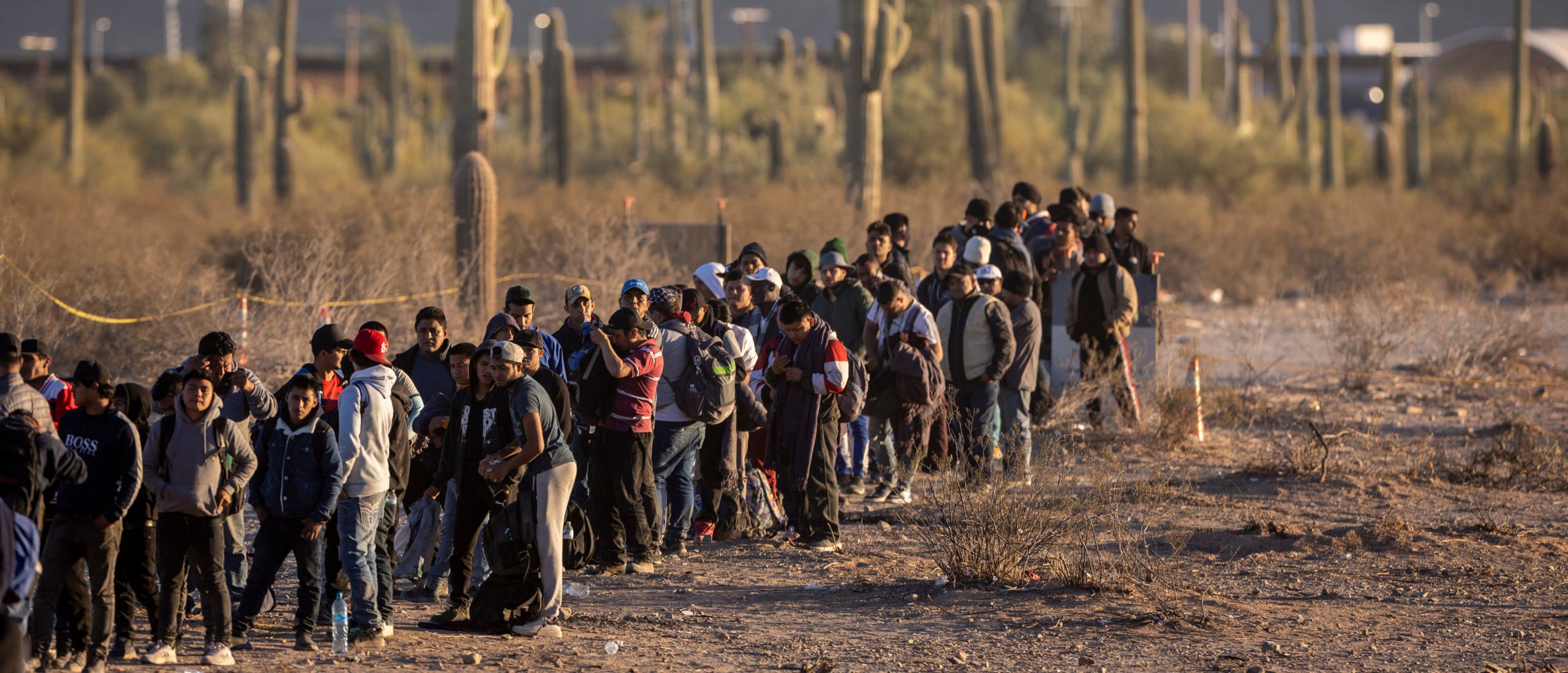 LUKEVILLE, ARIZONA - DECEMBER 07: Immigrants line up at a remote U.S. Border Patrol processing center after crossing the U.S.-Mexico border on December 07, 2023 in Lukeville, Arizona. (Photo by John Moore/Getty Images)