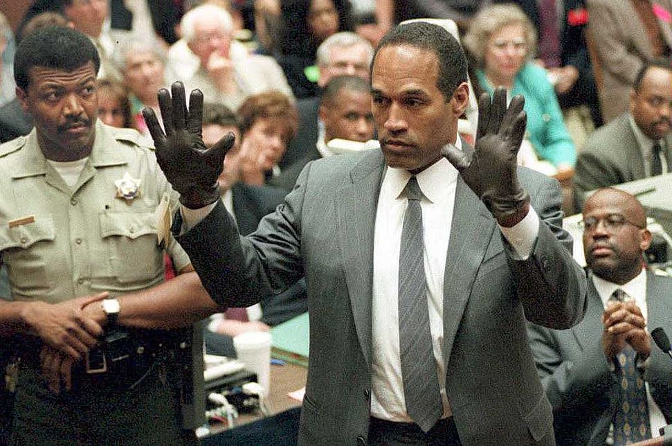 LOS ANGELES, CA - JUNE 21: O.J. Simpson shows the jury a new pair of Aris extra-large gloves, similar to the gloves found at the Bundy and Rockingham crime scene 21 June 1995, during his double murder trial in Los Angeles,CA. Deputy Sheriff Roland Jex(L) and Prosecutor Christopher Darden (R) look on. (Photo credit should read VINCE BUCCI/AFP via Getty Images)