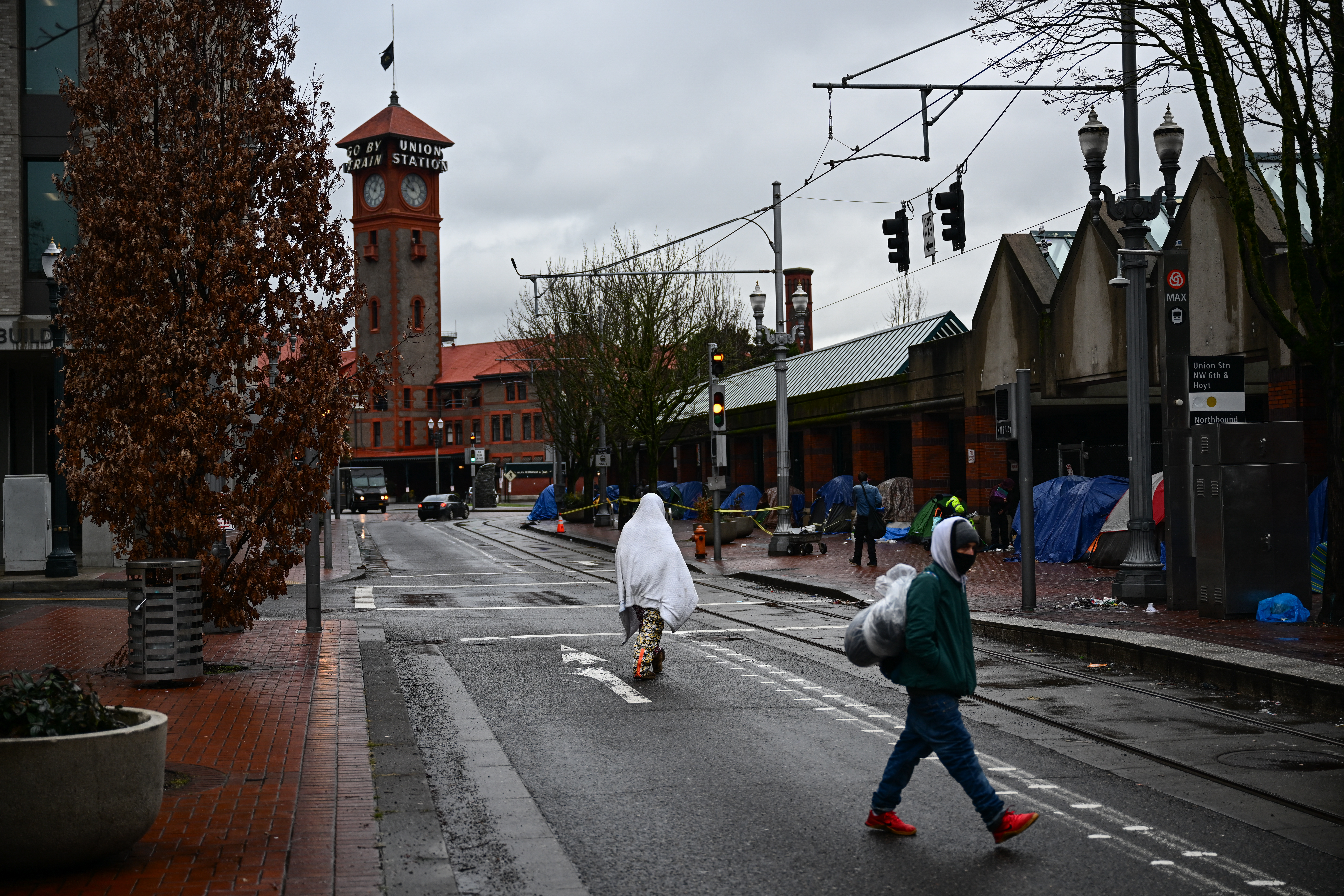 A person walks covered with a blanket past an encampment of tents on the street near Union Station in Portland, Oregon on January 24, 2024. In the midst of a presidential election year, Portland's decline is brandished by the conservative press depicting a city ravaged by its progressive ideals, in a state controlled by the left for over 40 years. (Photo by Patrick T. Fallon / AFP) (Photo by PATRICK T. FALLON/AFP via Getty Images)
