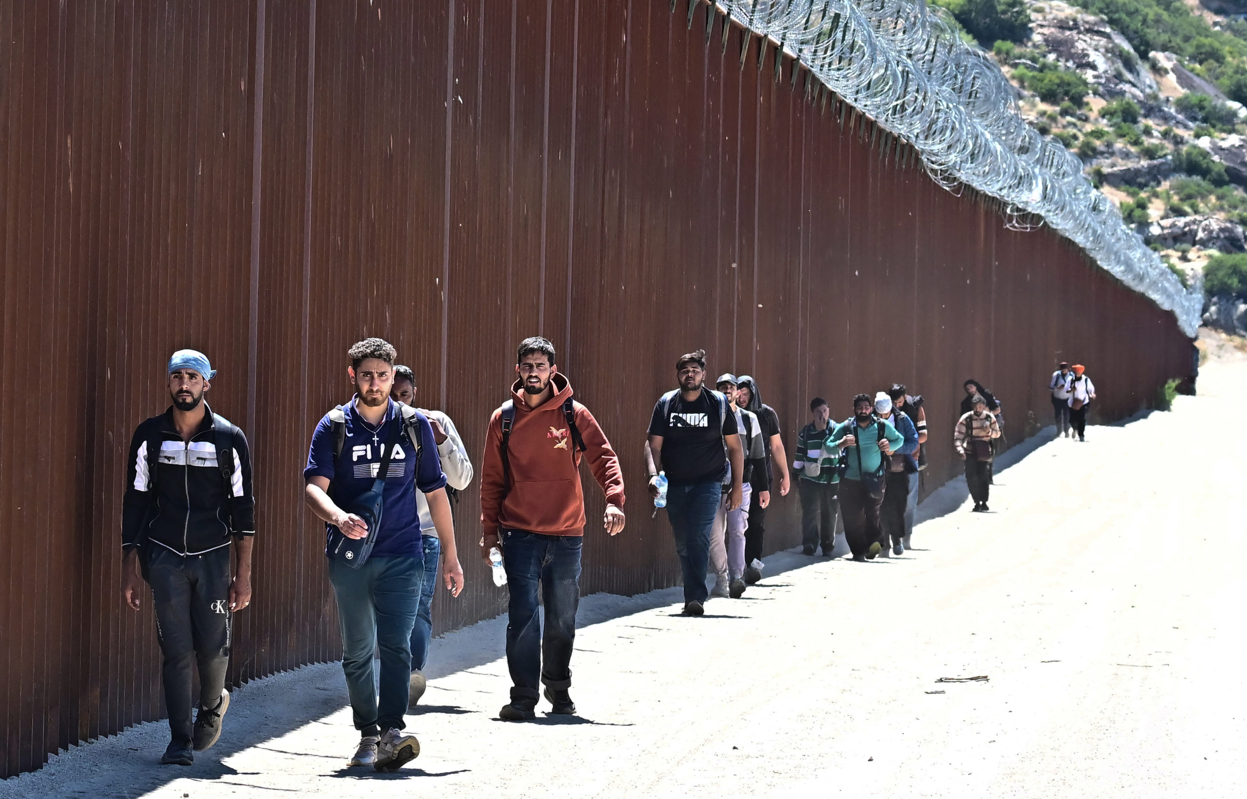 Migrants walk on the US side of the border wall in Jacumba Hot Springs, California on June 5, 2024, after walking across from Mexico. Migrants from countries such as Turkey, Jordan, Guatemala, Nicaragua, China and India made their way on foot into the United States today before being met with by Customs and Border Patrol agents for processing. The United States will temporarily close its Mexico border to asylum seekers starting today, June 5, as President Joe Biden as tries to neutralize his political weakness on migration ahead of November's election battle with Donald Trump. The 81-year-old Democrat signed a long-awaited executive order taking effect at midnight to "gain control" of the southern frontier with Mexico, after record numbers of illegal border crossings sparked concerns among voters. (Photo by FREDERIC J. BROWN/AFP via Getty Images)