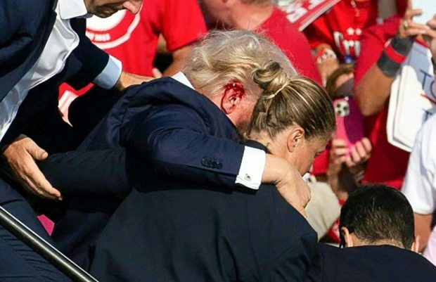 TOPSHOT - Republican candidate Donald Trump is seen with blood on his face surrounded by secret service agents as he is taken off the stage at a campaign event at Butler Farm Show Inc. in Butler, Pennsylvania, July 13, 2024. Republican candidate Donald Trump was evacuated from the stage at today's rally after what sounded like shots rang out at the event in Pennsylvania, according to AFP. The former US president was seen with blood on his right ear as he was surrounded by security agents, who hustled him off the stage as he pumped his first to the crowd. Trump was bundled into an SUV and driven away. (Photo by Rebecca DROKE / AFP) (Photo by REBECCA DROKE/AFP via Getty Images)