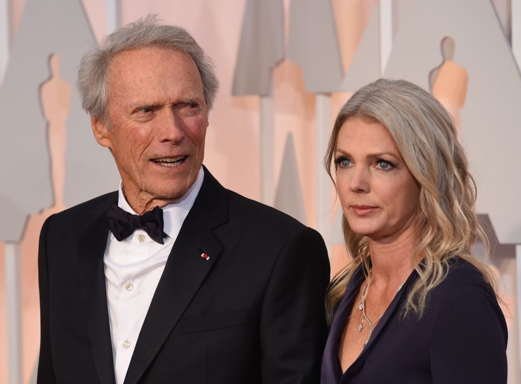 Nominee for Best Picture "American Sniper," Clint Eastwood (L) and Christina Sandera pose on the red carpet for the 87th Oscars on February 22, 2015 in Hollywood, California. AFP PHOTO / MARK RALSTON (Photo by MARK RALSTON / AFP) (Photo by MARK RALSTON/AFP via Getty Images)