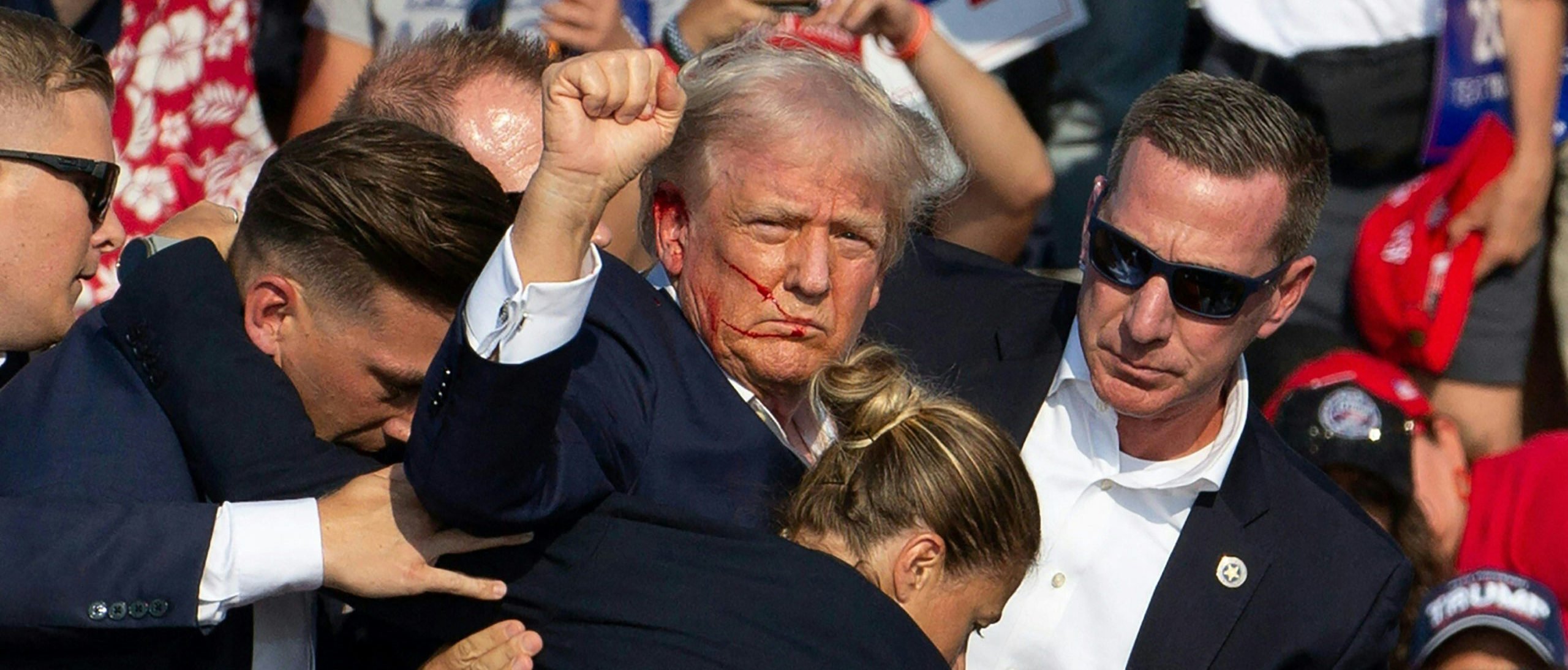 TOPSHOT - Republican candidate Donald Trump is seen with blood on his face surrounded by secret service agents as he is taken off the stage at a campaign event at Butler Farm Show Inc. in Butler, Pennsylvania, July 13, 2024. Donald Trump was hit in the ear in an apparent assassination attempt by a gunman at a campaign rally on Saturday, in a chaotic and shocking incident that will fuel fears of instability ahead of the 2024 US presidential election. The 78-year-old former president was rushed off stage with blood smeared across his face after the shooting in Butler, Pennsylvania, while the gunman and a bystander were killed and two spectators critically injured. (Photo by Rebecca DROKE / AFP) (Photo by REBECCA DROKE/AFP via Getty Images)