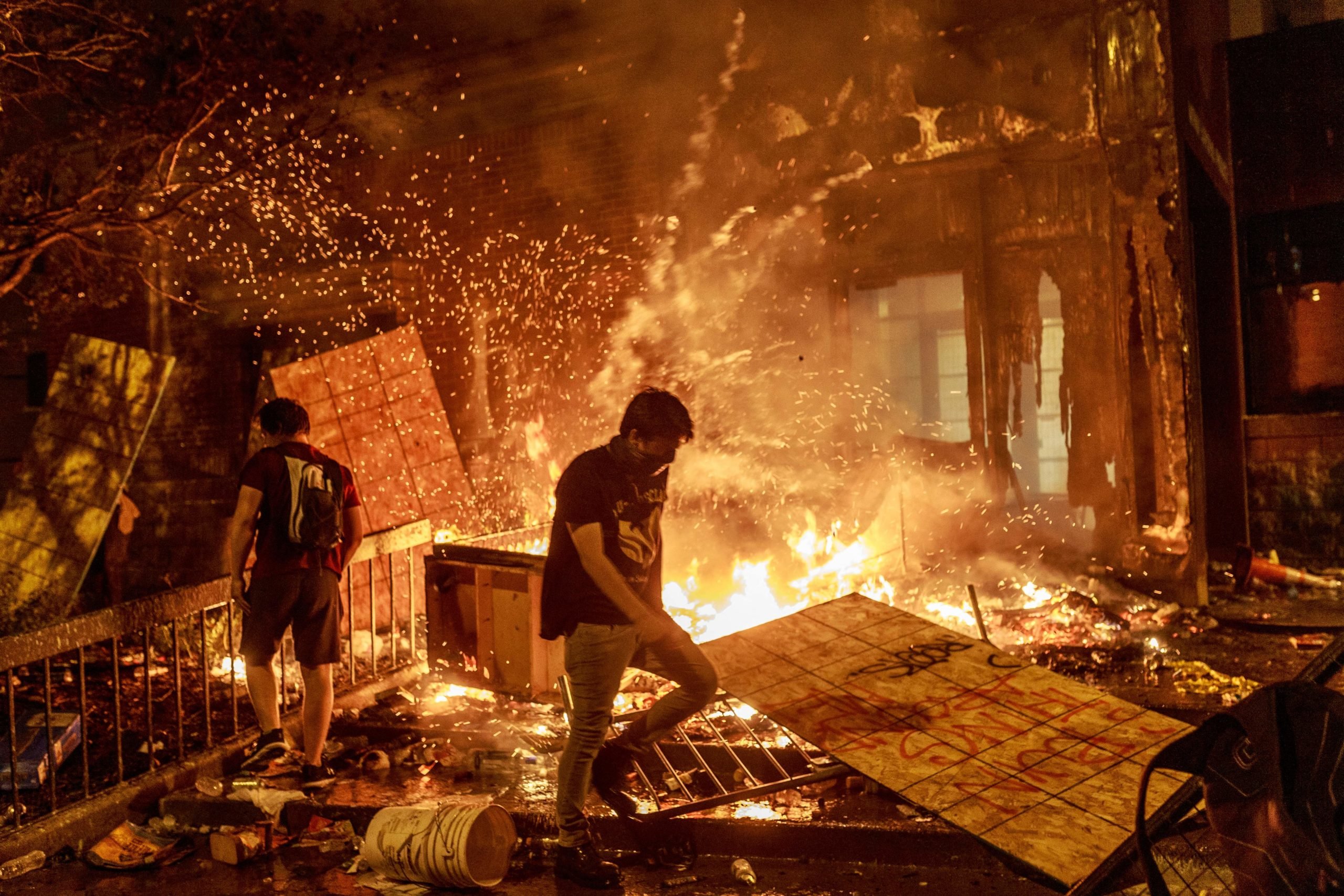 TOPSHOT - Protesters walk past burning debris outside the Third Police Precinct on May 28, 2020 in Minneapolis, Minnesota, during a protest over the death of George Floyd, an unarmed black man, who died after a police officer kneeled on his neck for several minutes. A police precinct in Minnesota went up in flames late on May 28 in a third day of demonstrations as the so-called Twin Cities of Minneapolis and St. Paul seethed over the shocking police killing of a handcuffed black man. The precinct, which police had abandoned, burned after a group of protesters pushed through barriers around the building, breaking windows and chanting slogans. A much larger crowd demonstrated as the building went up in flames. EREM YUCEL/AFP via Getty Images