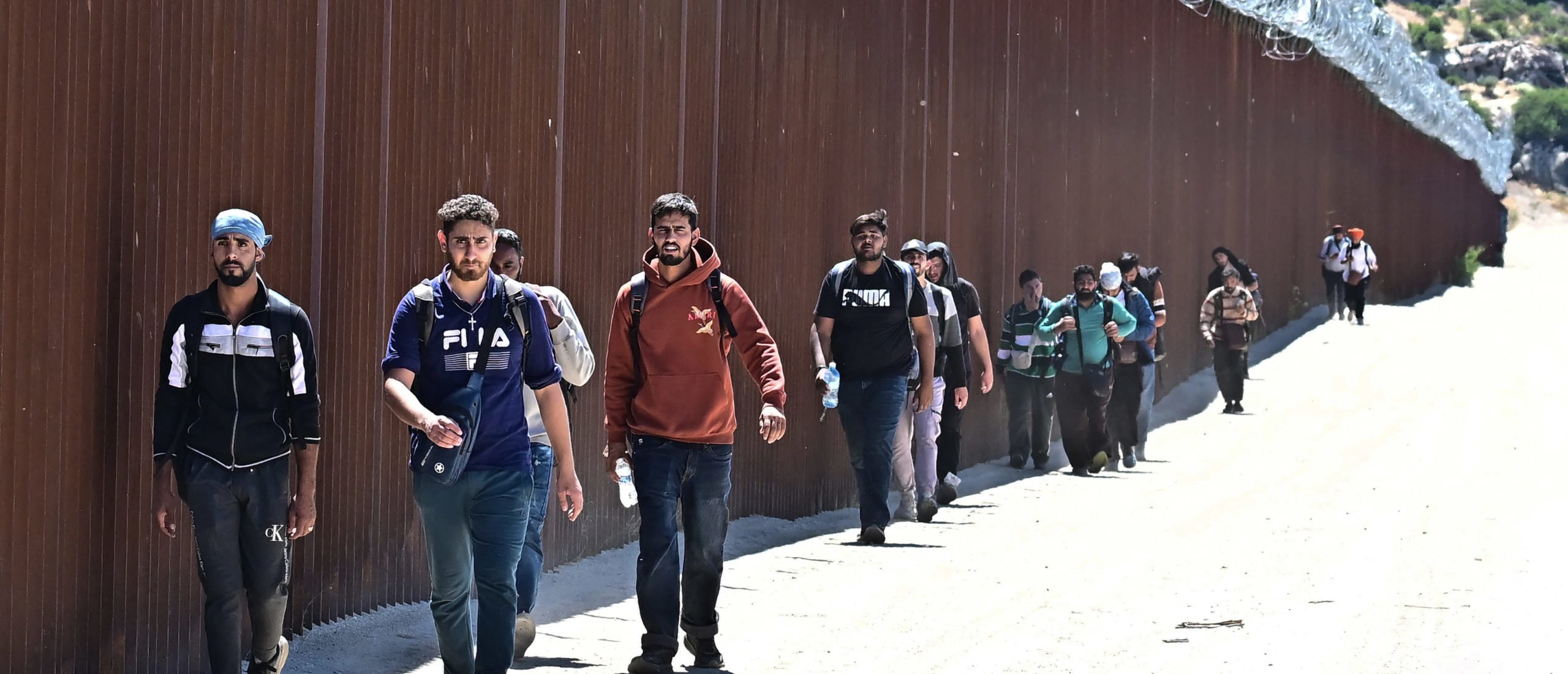 Migrants walk on the US side of the border wall in Jacumba Hot Springs, California on June 5, 2024, after walking across from Mexico. Migrants from countries such as Turkey, Jordan, Guatemala, Nicaragua, China and India made their way on foot into the United States today before being met with by Customs and Border Patrol agents for processing. The United States will temporarily close its Mexico border to asylum seekers starting today, June 5, as President Joe Biden as tries to neutralize his political weakness on migration ahead of November's election battle with Donald Trump. The 81-year-old Democrat signed a long-awaited executive order taking effect at midnight to "gain control" of the southern frontier with Mexico, after record numbers of illegal border crossings sparked concerns among voters. (Photo by Frederic J. BROWN / AFP)