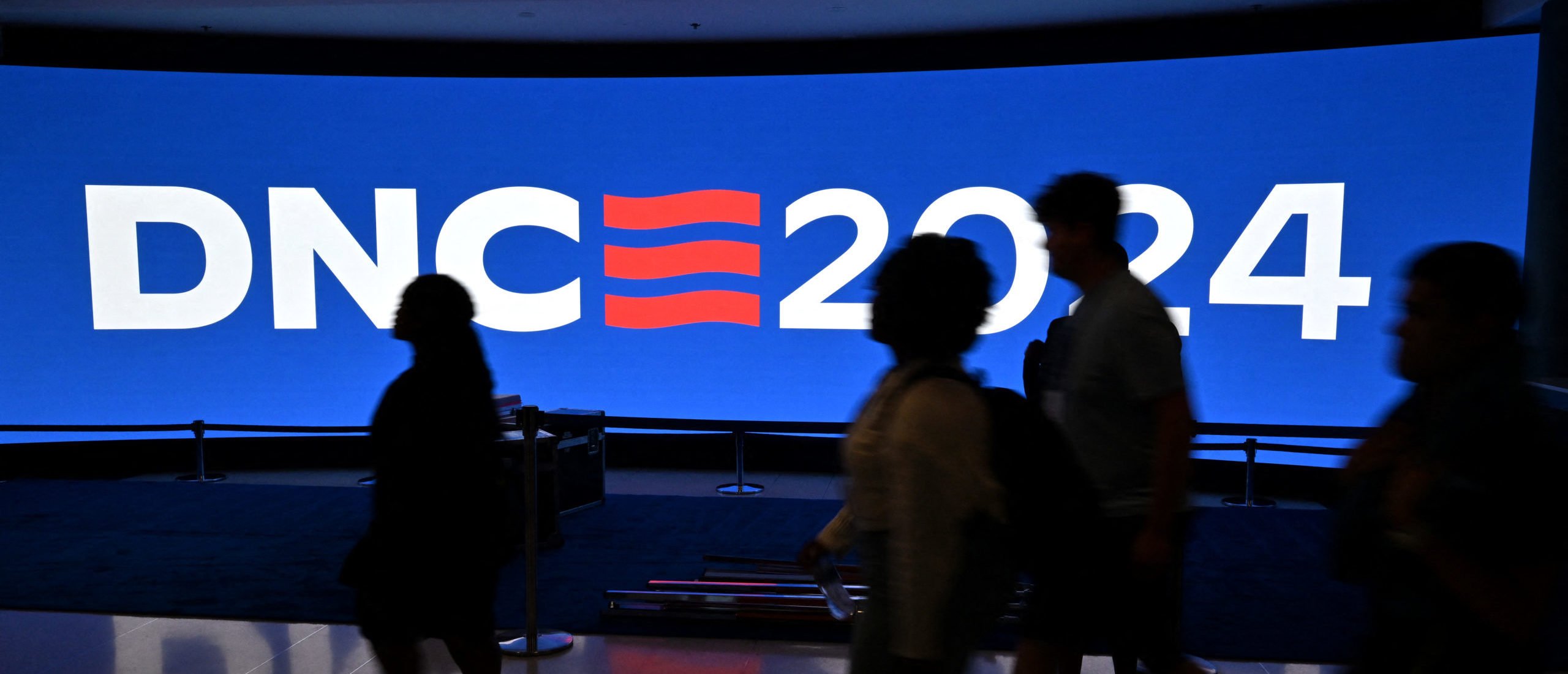 People walk past a screen before the Democratic National Convention (DNC) at the United Center in Chicago, Illinois, on August 15, 2024. Vice President Kamala Harris will formally accept the party's nomination as presidential candidate at the DNC, which will be held in Chicago from August 19-22. (Photo by Robyn Beck / AFP) (Photo by ROBYN BECK/AFP via Getty Images)