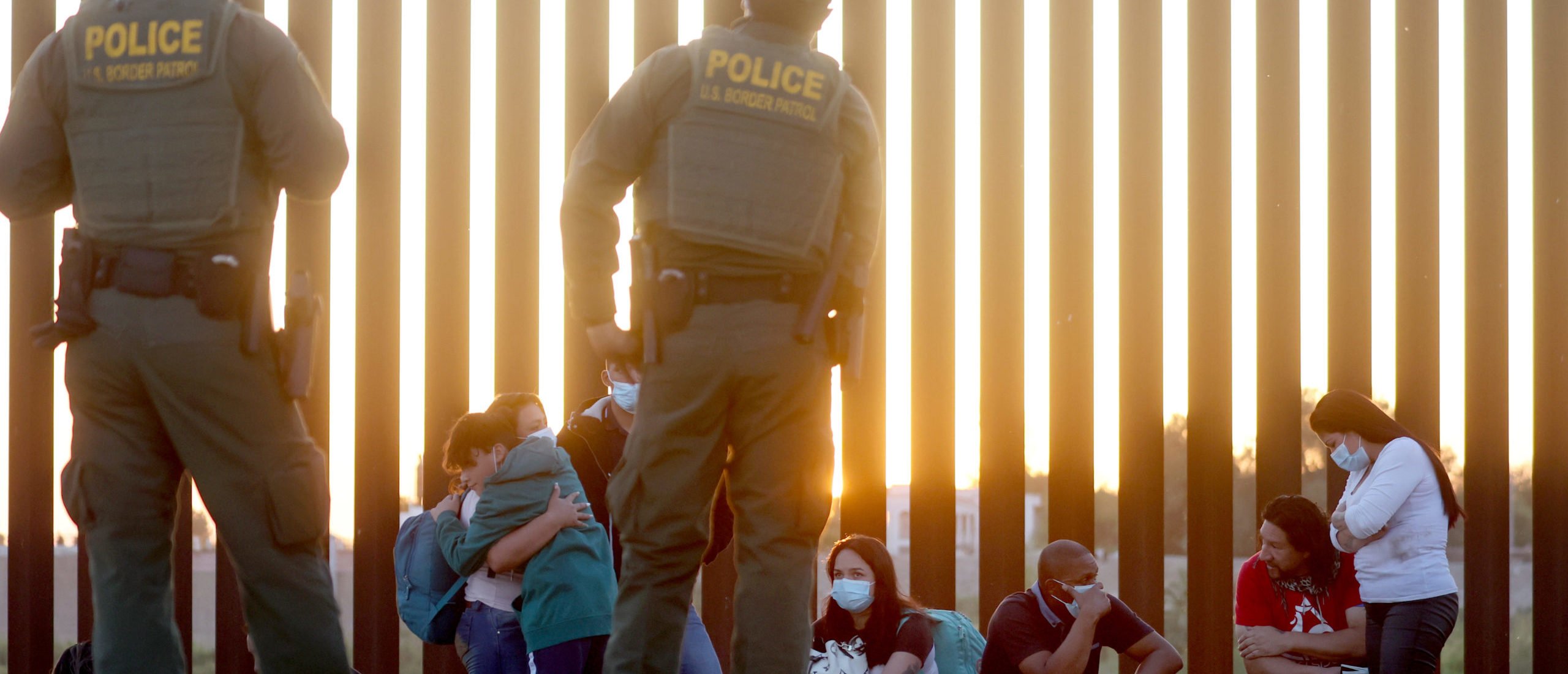 U.S. Border Patrol agents keep watch as immigrants wait to board a U.S. Border Patrol bus to be taken for processing after crossing the border from Mexico on May 18, 2022 in Yuma, Arizona. Title 42, the controversial pandemic-era border policy enacted by President Trump, which cites COVID-19 as the reason to rapidly expel asylum seekers at the U.S. border, is set to officially expire on May 23rd. A federal judge in Louisiana is expected to deliver a ruling this week on whether the Biden administration can lift Title 42. (Photo by Mario Tama/Getty Images)